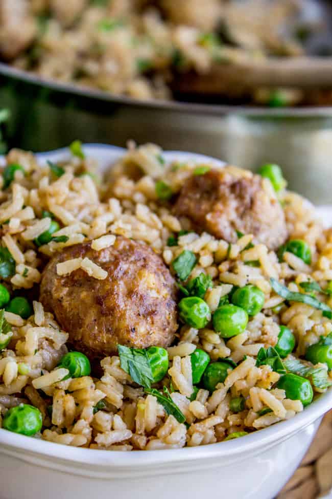 homemade meatballs with rice and peas garnished with fresh parsley in a white bowl. 