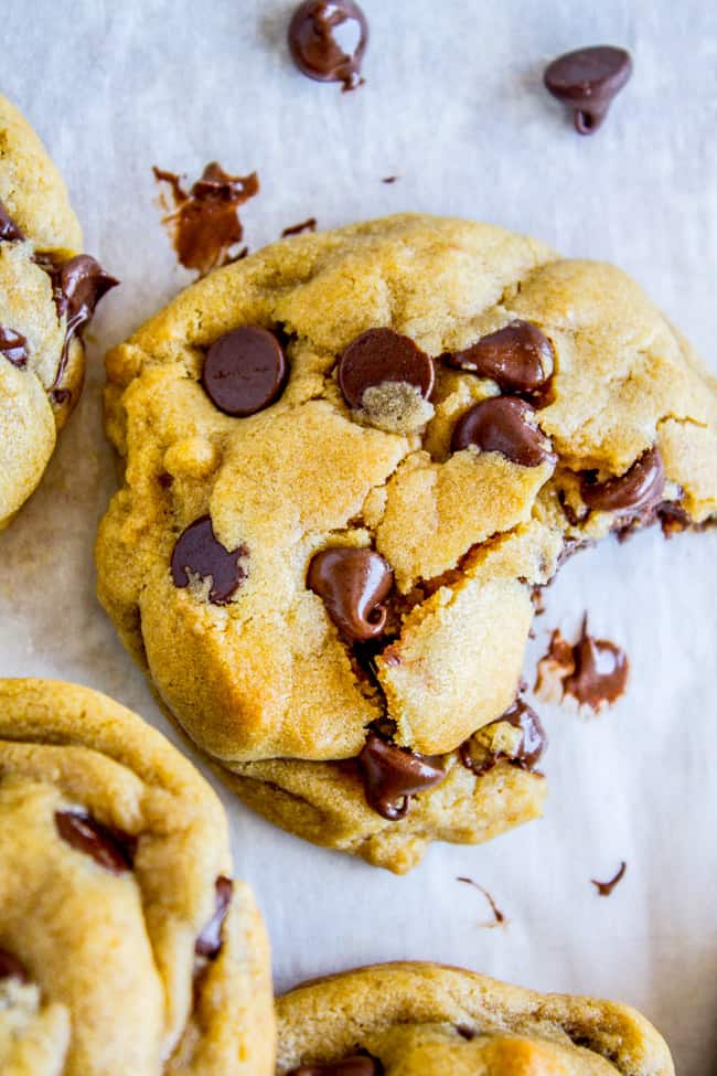 chocolate chip cookies on parchment paper, one with a big bite taken out of it.