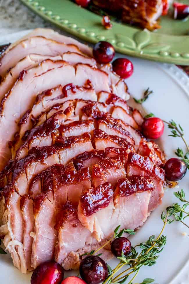 Sliced glazed ham on a white plate with Cranberries and thyme