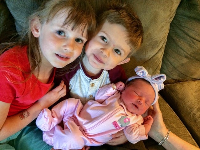 Two young children holding their newborn baby sister.