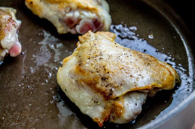 Sauteeing a chicken thigh in a skillet.