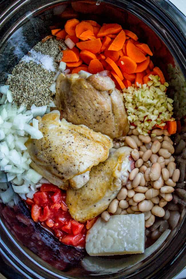 Prepped chicken, beans, parmesan rind, spices, and veggies in crockpot.