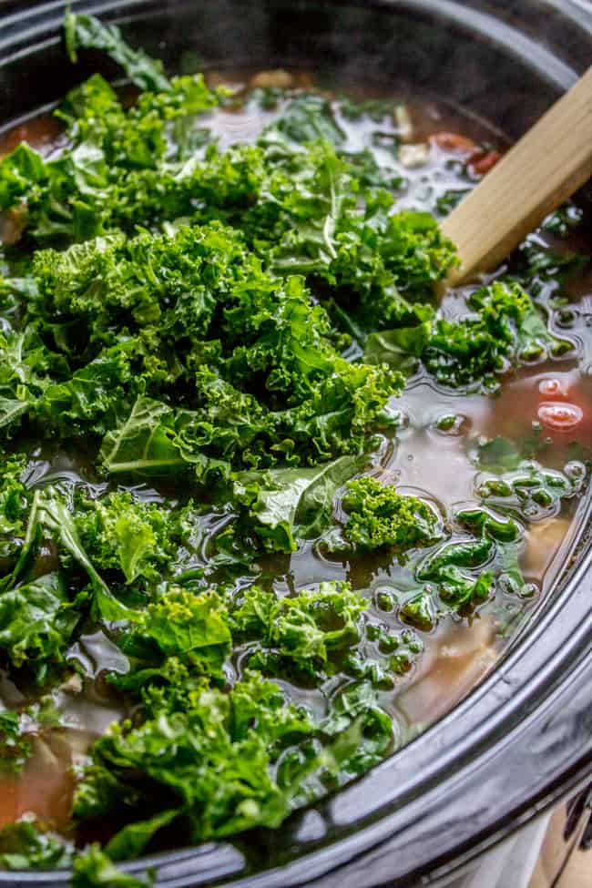 Adding kale to a slow cooker.