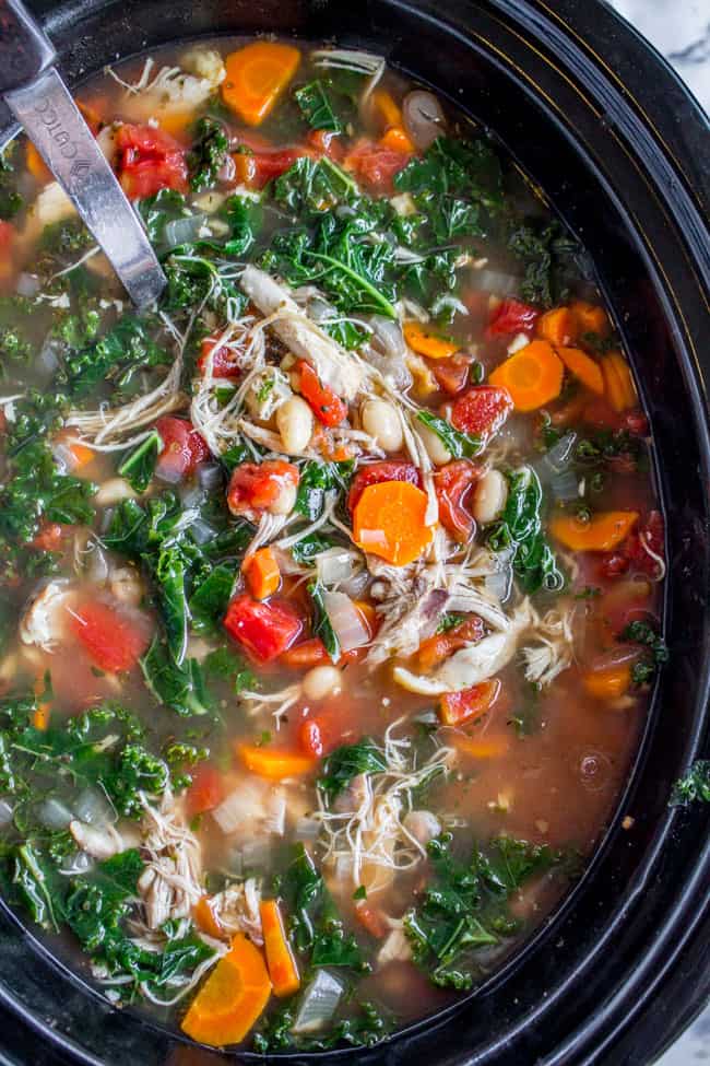 a metal spoon in a slow cooker of white bean, chicken, and kale soup.