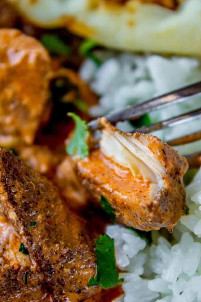 a fork tearing a bite of chicken tikka masala on a bed of rice. 