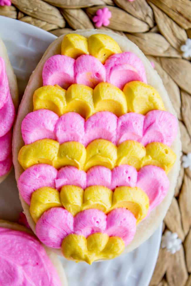 Sugar Cookies Recipe showing an egg-shaped soft sugar cookie with dollops of pink and yellow butter cream frosting