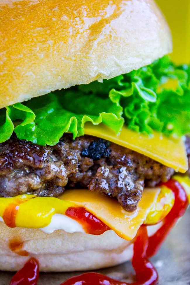 close up shot of juicy smash burger with cheese, lettuce, and dripping with ketchup and mustard.