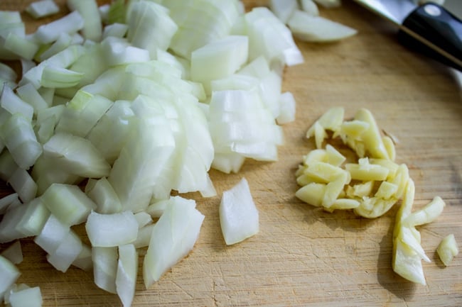 chopped onions and garlic on a wooden cutting board.