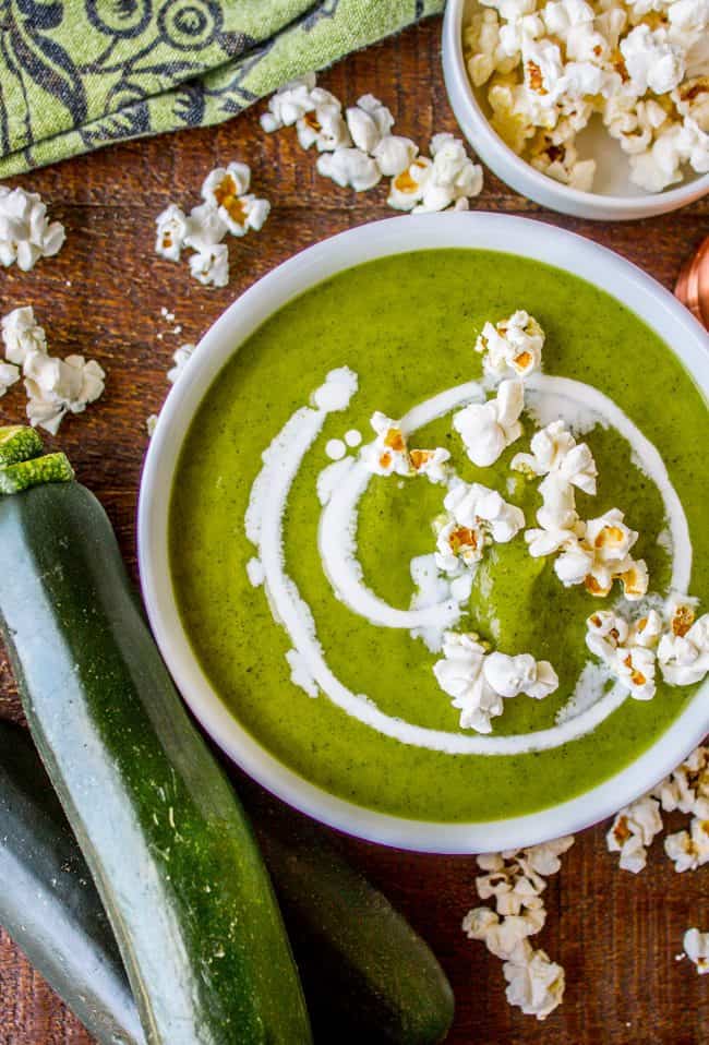 a bowl of zucchini soup with a swirl of cream, topped with plain popcorn. 