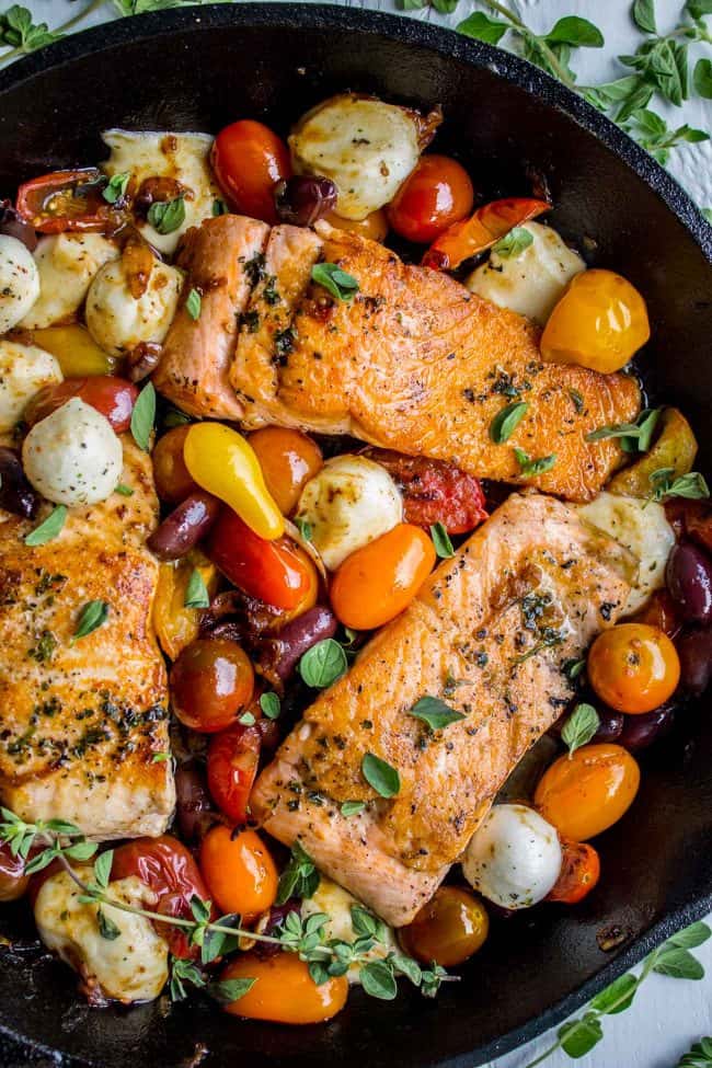 pan seared salmon with mix of assorted cherry tomatoes and roasted mozzarella balls in iron skillet.