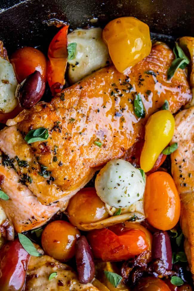 Salmon filet in cast iron skillet cooked with cherry tomatoes, mozzarella balls, and kalamata olice.