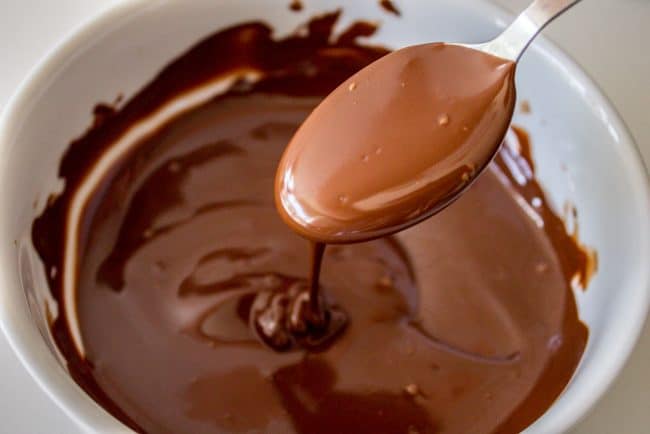 melted chocolate dripping from a spoon into a white bowl.