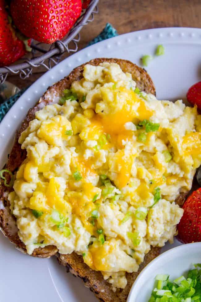 scrambled eggs on whole grain toast with fresh strawberries on a white plate.