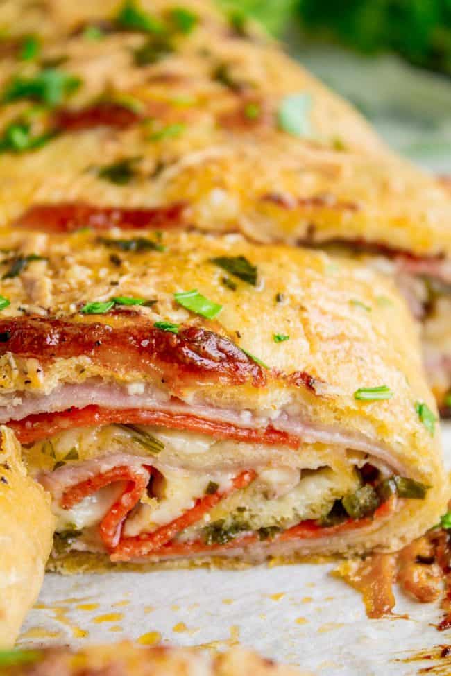 Sliced stromboli sandwich filled with meat and cheese topped with fresh parsley.