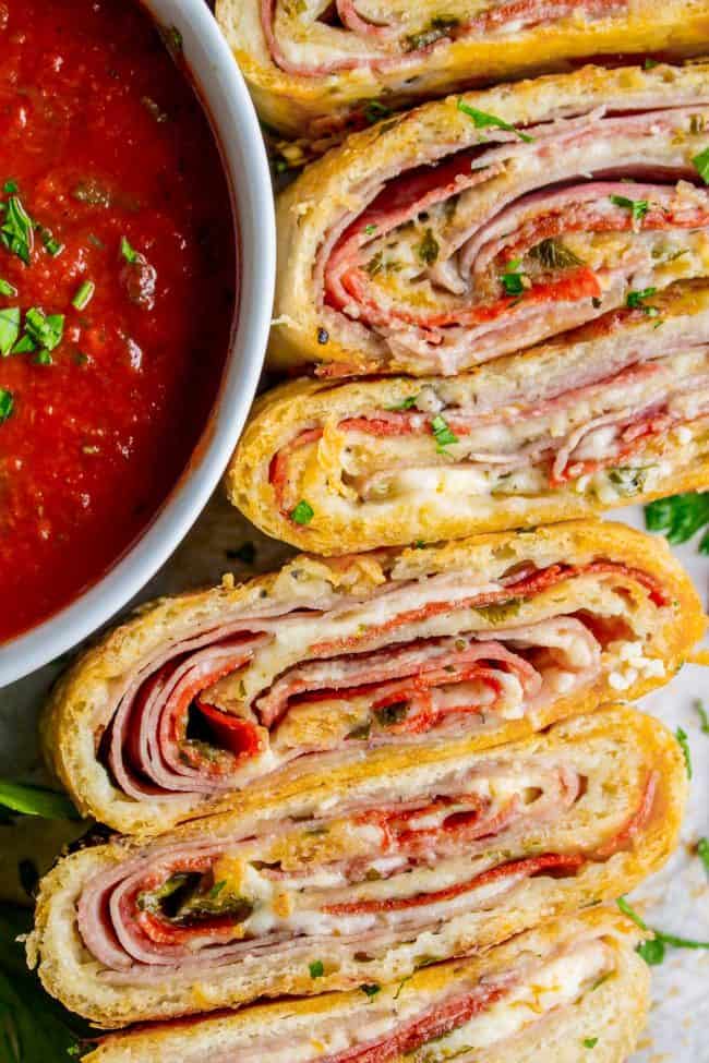 sliced stromboli with meat, cheese, and fresh parsley next to a bowl of marinara sauce.