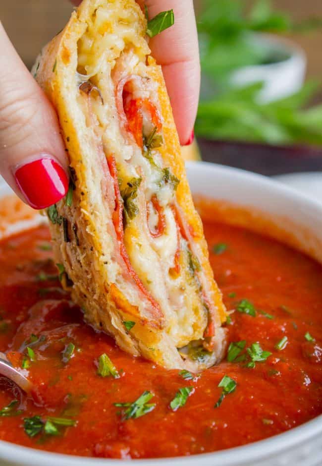 Manicured hand dipping stromboli slice in marinara sauce.