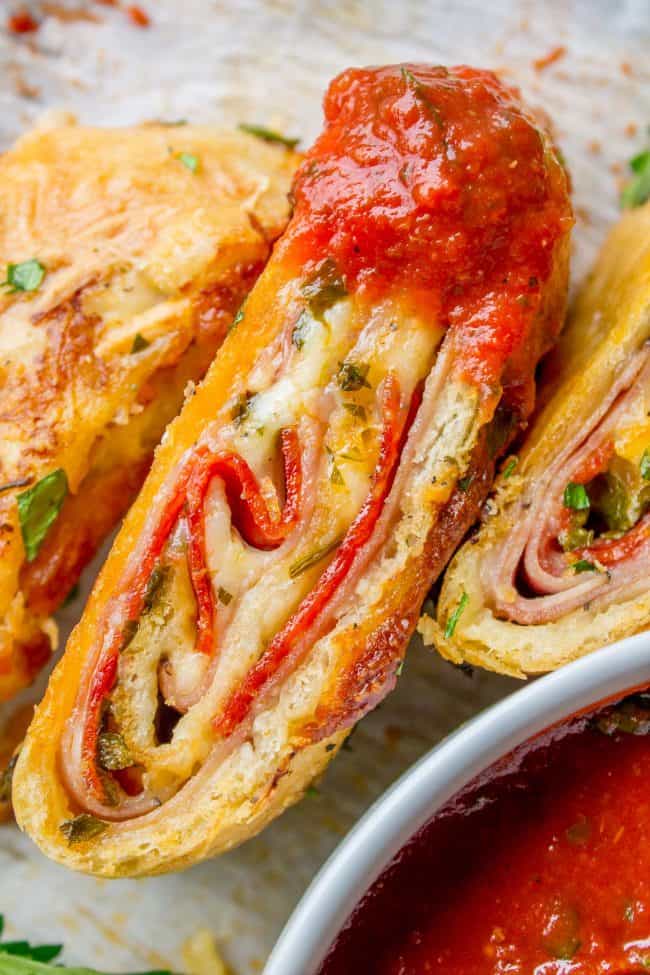 Sliced meat and cheese filled stromboli sandwich dipped in marinara sauce.