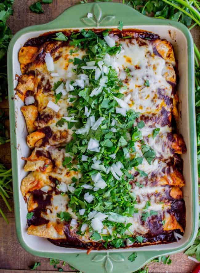 sweet potato and black bean enchiladas topped with cilantro and onions in a baking dish. 