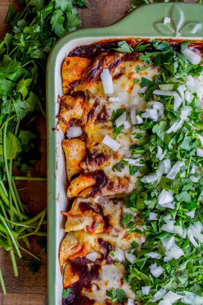 sweet potato and black bean enchiladas topped with chopped onions and cilantro in a baking dish. 