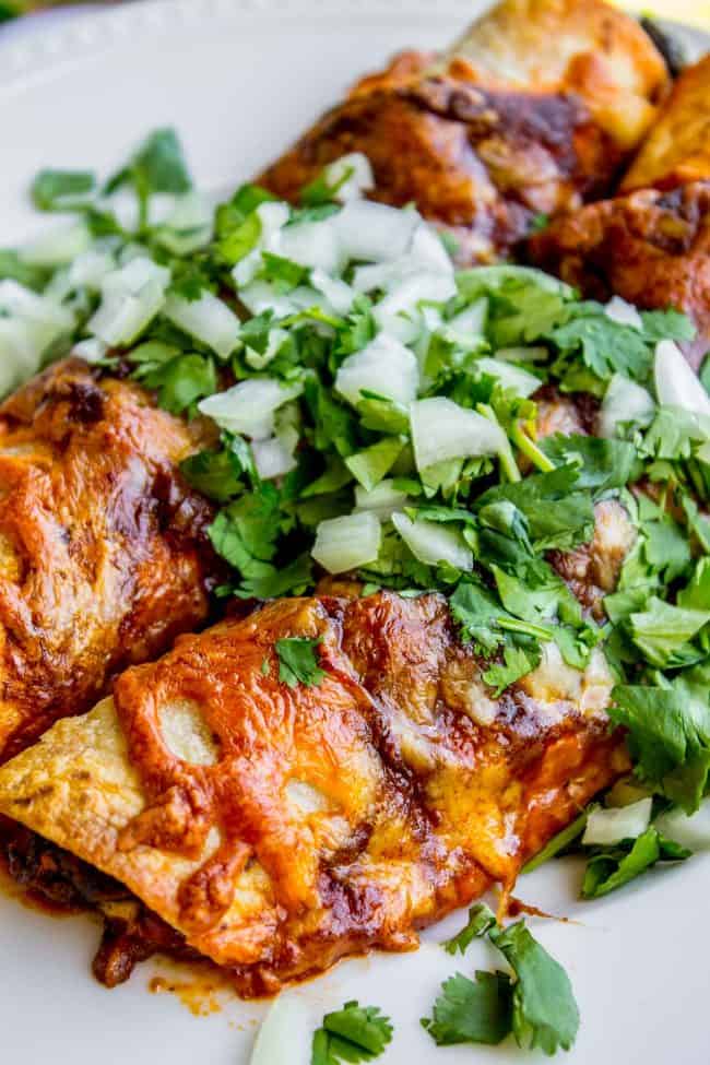 sweet potato and black bean enchiladas topped with cilantro and onions on a plate.