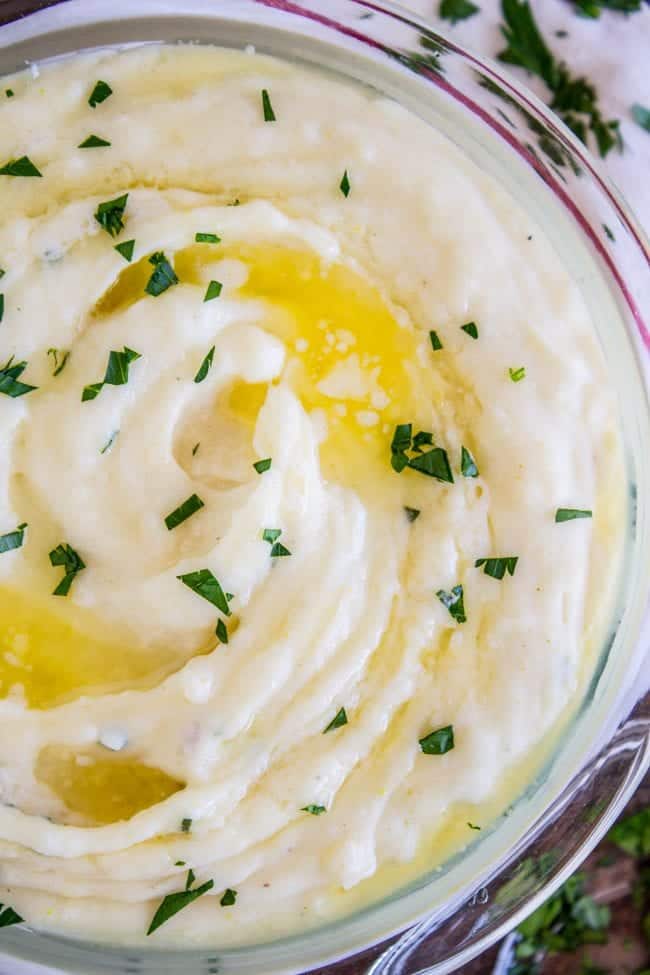 creamy mashed potatoes in a glass bowl with melted butter and parsley on top.