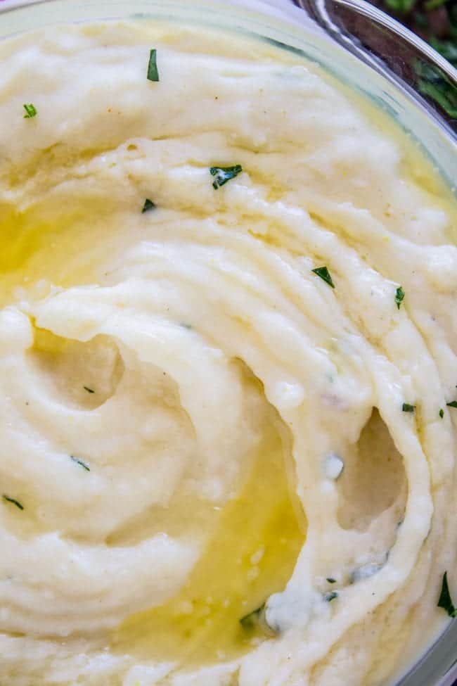 a glass bowl of creamy mashed potatoes with butter and parsley.