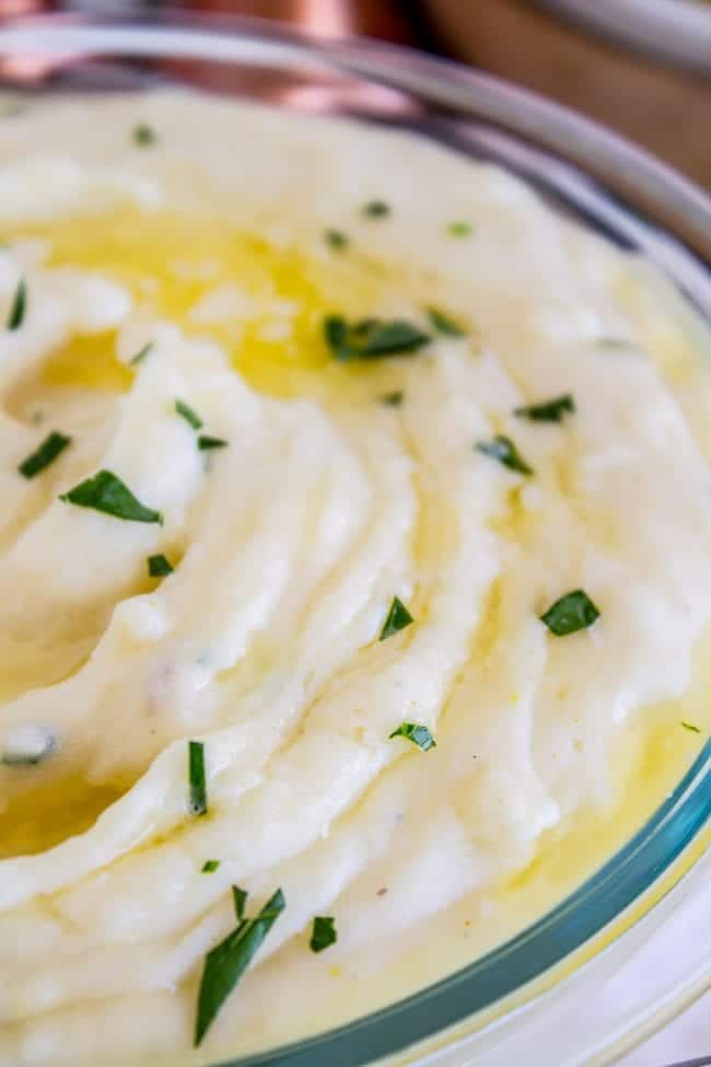 creamy mashed potatoes with butter and parsley on top in a glass bowl.