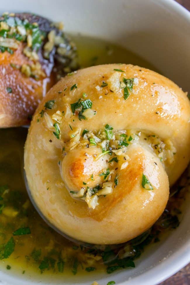 fresh homemade garlic knots being soaked in garlic parsley butter.