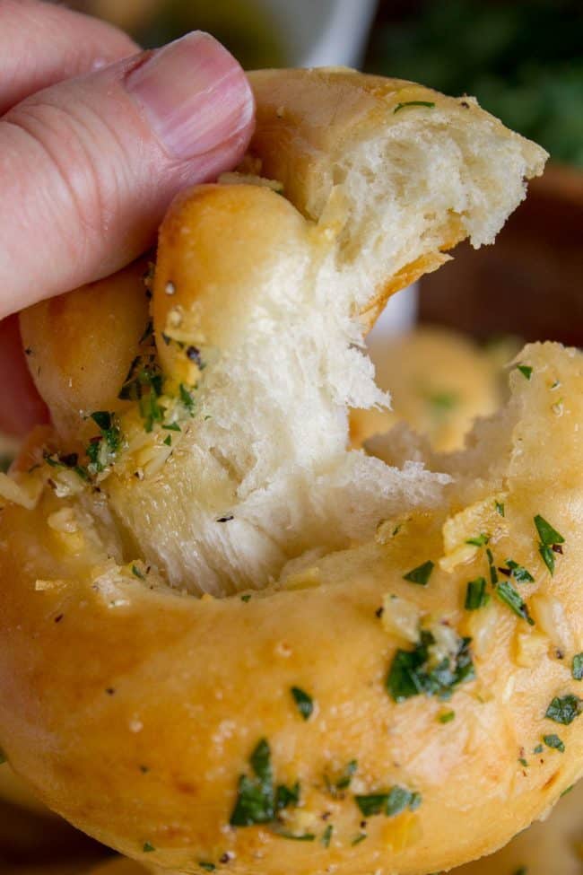 a hand tearing open a homemade garlic knots with parsley garlic butter.