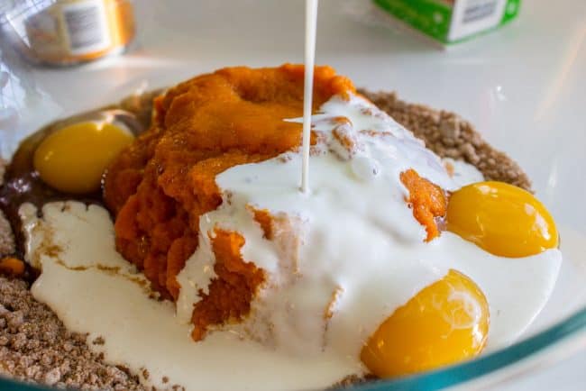 pouring cream into a bowl with pumpkin, eggs, and other ingredients for pumpkin pie filling. 