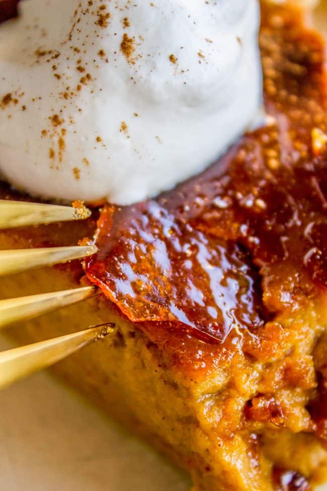 A fork touching the creme brulee topping on a creamy pumpkin pie with whipped cream.