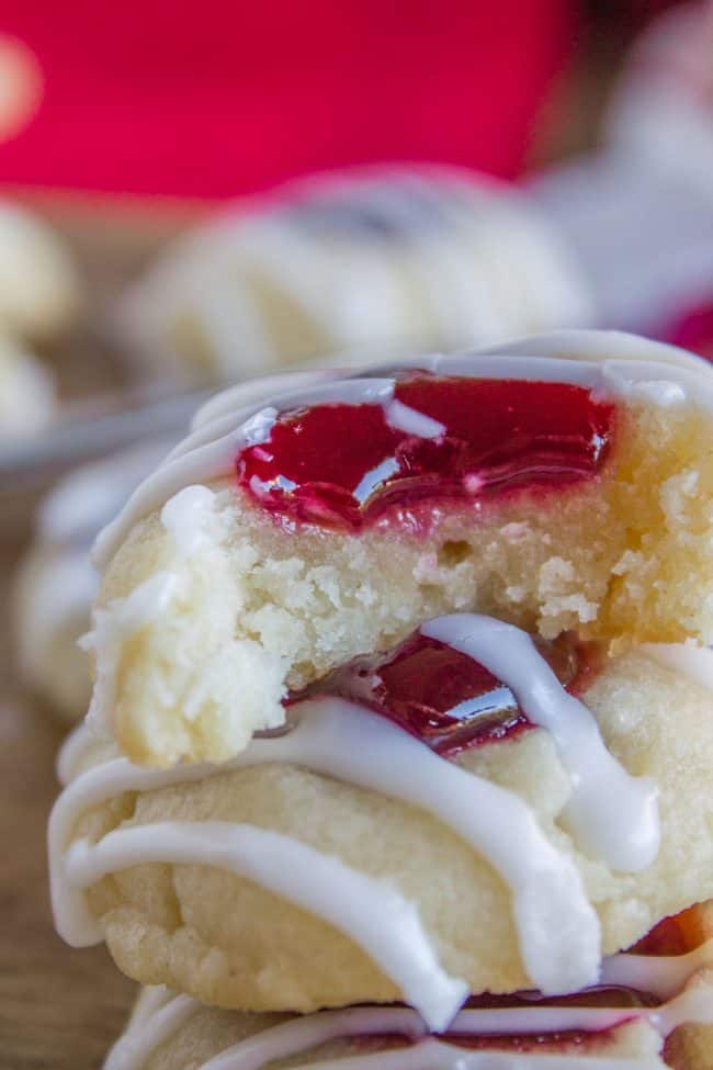 Raspberry Thumbprint Cookies with icing in a stack, the top cookie with a bite missing.