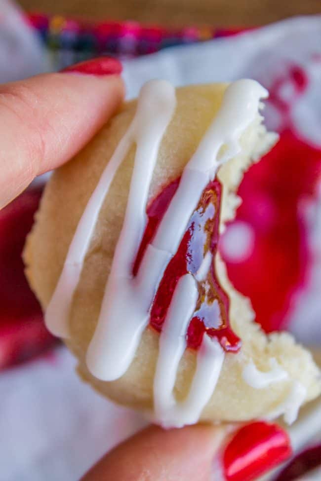 Glaze-drizzled shortbread thumbprint cookie with bite taken, held by manicured hand.