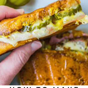 A hand holds a Cubano sandwich filled with pickles, melted cheese, and meat. Sliced pickles and an orange slice sit in the background, with text below that highlights traditional Cuban sandwiches.