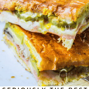 Close-up of two stacked Cuban sandwiches with melted cheese, ham, pickles, and crispy toasted bread. Text at the bottom reads, “Seriously the Finest Homemade Cubanos – The Food Charlatan.”.