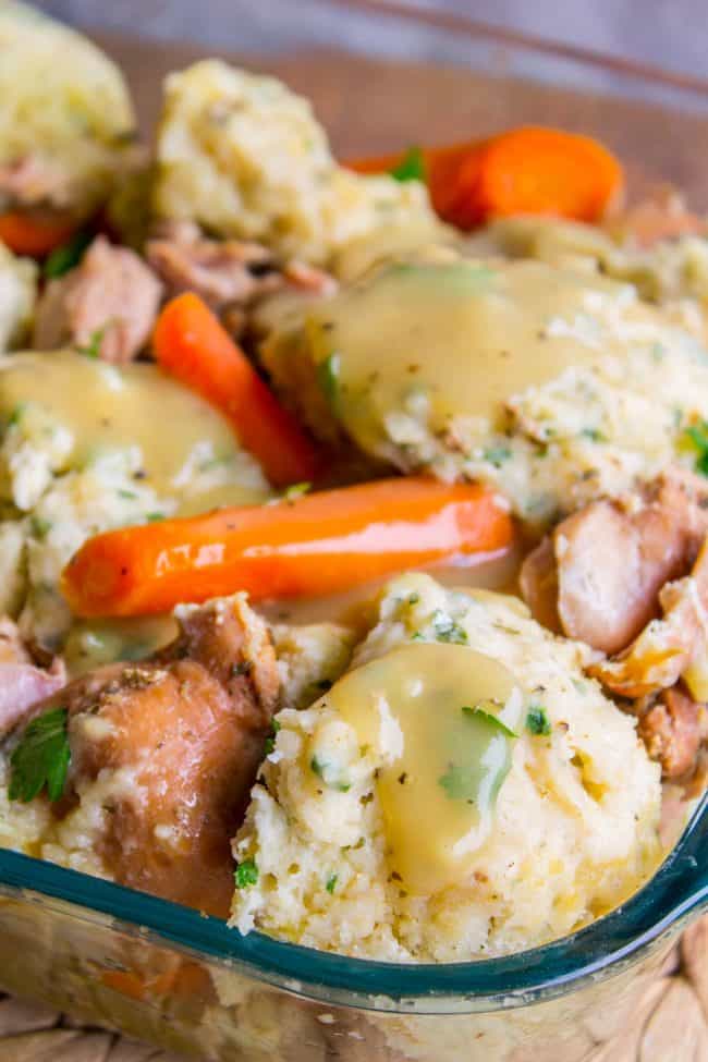 chicken and dumplings with carrots in a glass baking dish with gravy on top. 