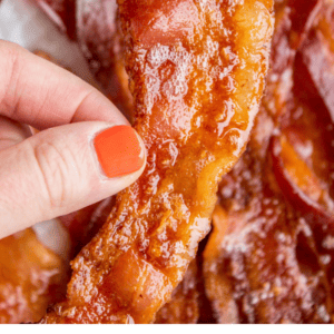 lifting a crispy piece of bacon from a sheet pan.