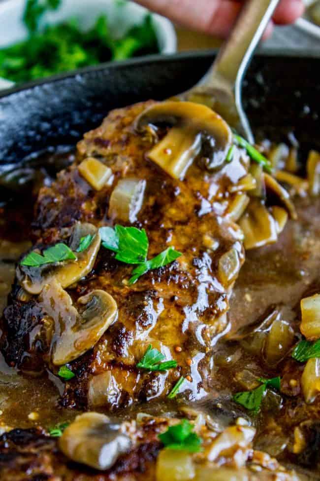 salisbury steak with mushroom gravy and fresh parsley in a cast iron skillet.