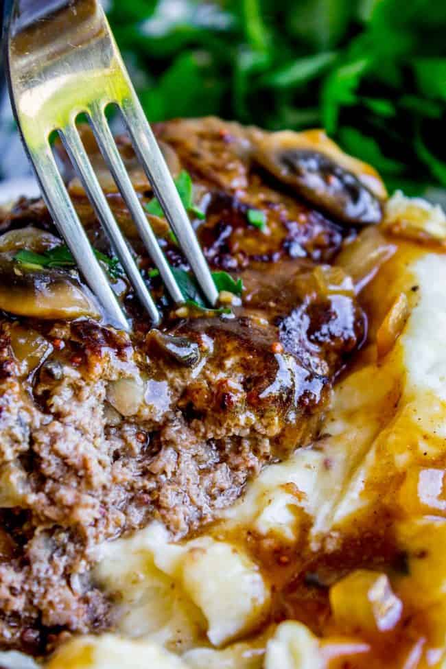 salisbury steak with mushroom gravy on a creamy mashed potatoes with a fork lifting a bite.
