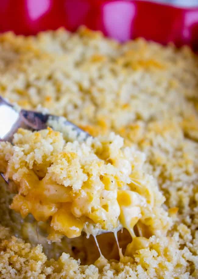 a metal spoon lifting a scoop of baked mac and cheese from the baking pan.