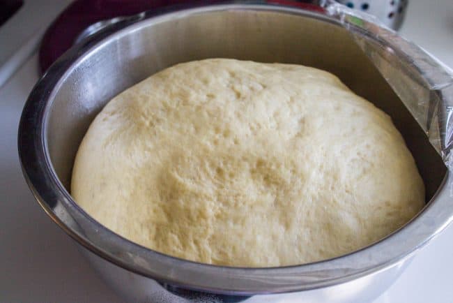 rising donut dough in a metal bowl.