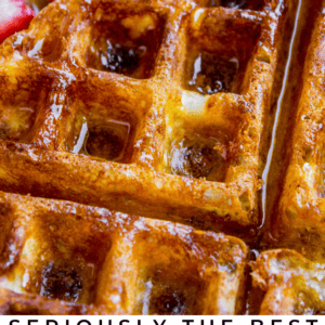 Close-up of golden brown waffles drizzled with syrup and topped with fresh strawberries and a fork. Text at the bottom reads: Seriously the Best Classic Waffles - The Food Charlatan.