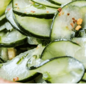 Close-up of thinly sliced cucumber salad with cilantro, lime, and red pepper flakes for a fresh, vibrant crunch. Text below reads: Fast & Fresh Cilantro-Lime Cucumber Salad. The Food Charlatan.