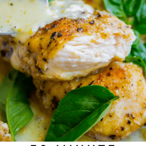 Close-up of a fork cutting into a juicy, seasoned chicken breast topped with creamy lemon basil sauce and fresh basil leaves. Text at the bottom reads: 30 Minute Stovetop Chicken with Lemon Basil Cream Sauce.