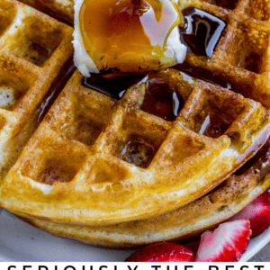 A close-up of a golden waffle topped with butter and drizzled with syrup, with strawberries and blueberries on the side. Text reads: Seriously Delicious Waffles – The Food Charlatan.
