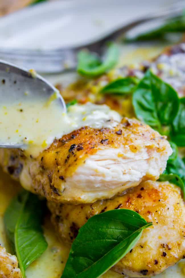 pan seared chicken with fresh basil and lemon cream sauce being poured on with a spoon.