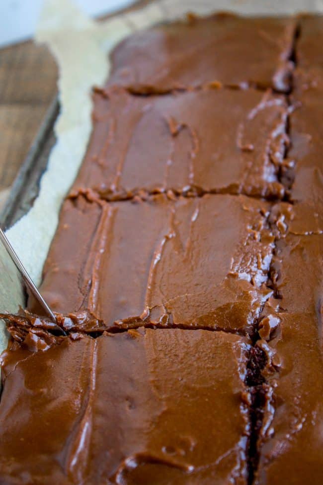 Texas chocolate sheet cake being cut into big slices with a butter knife.