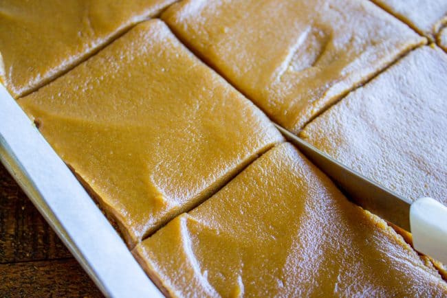 A knife cutting a frosted caramel cake recipe into squares