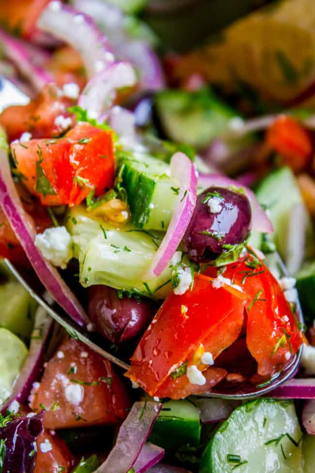 a spoon lifting a bite of Greek tomato cucumber salad with feta cheese.