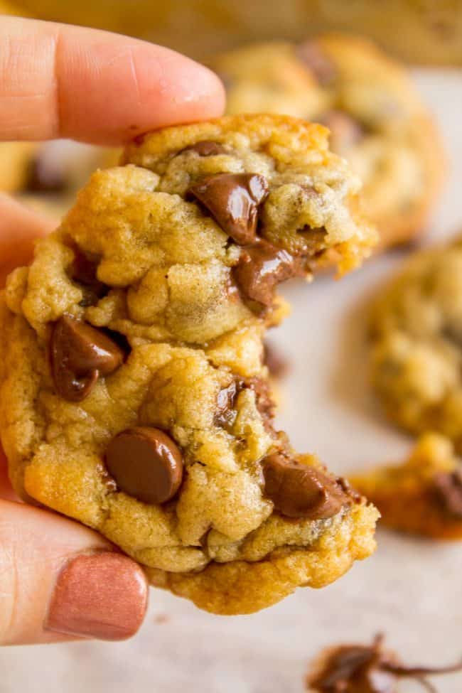 hand holding up a chocolate chip cookie with a big bite taken out of it. 